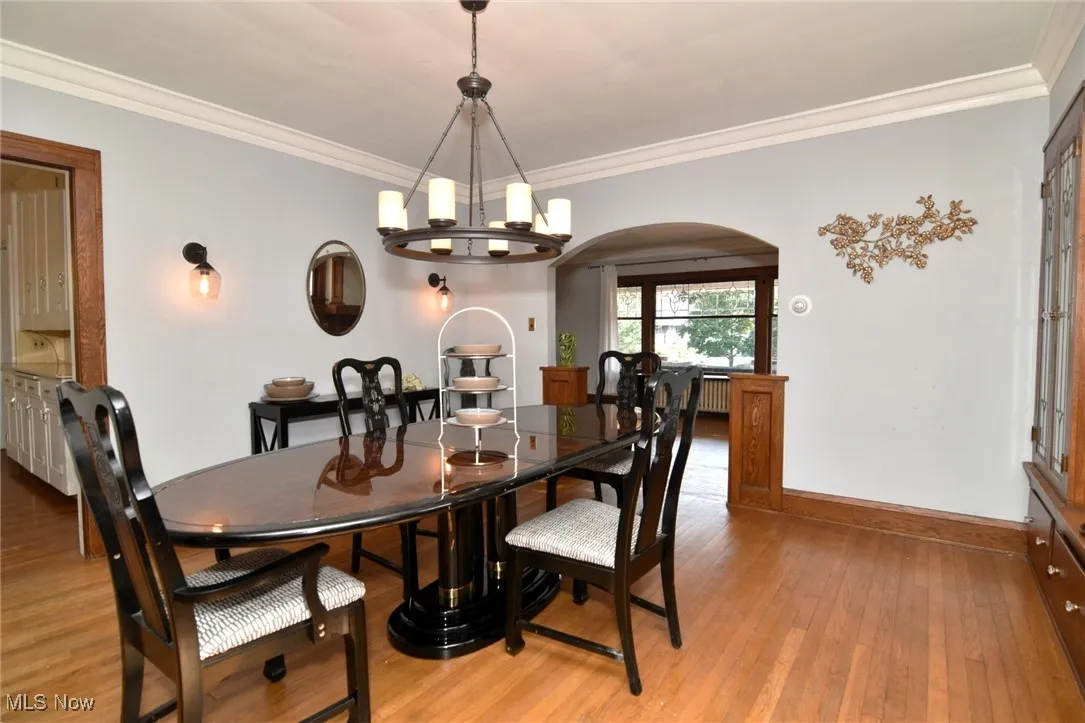 Dining room with arched walkways, a chandelier, light wood-style flooring, and crown molding