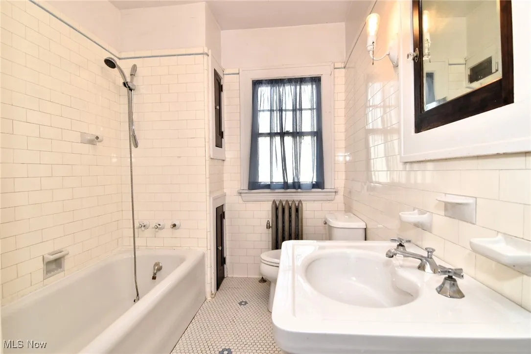 Full bathroom with radiator heating unit, bathing tub / shower combination, tile patterned floors, and tile walls