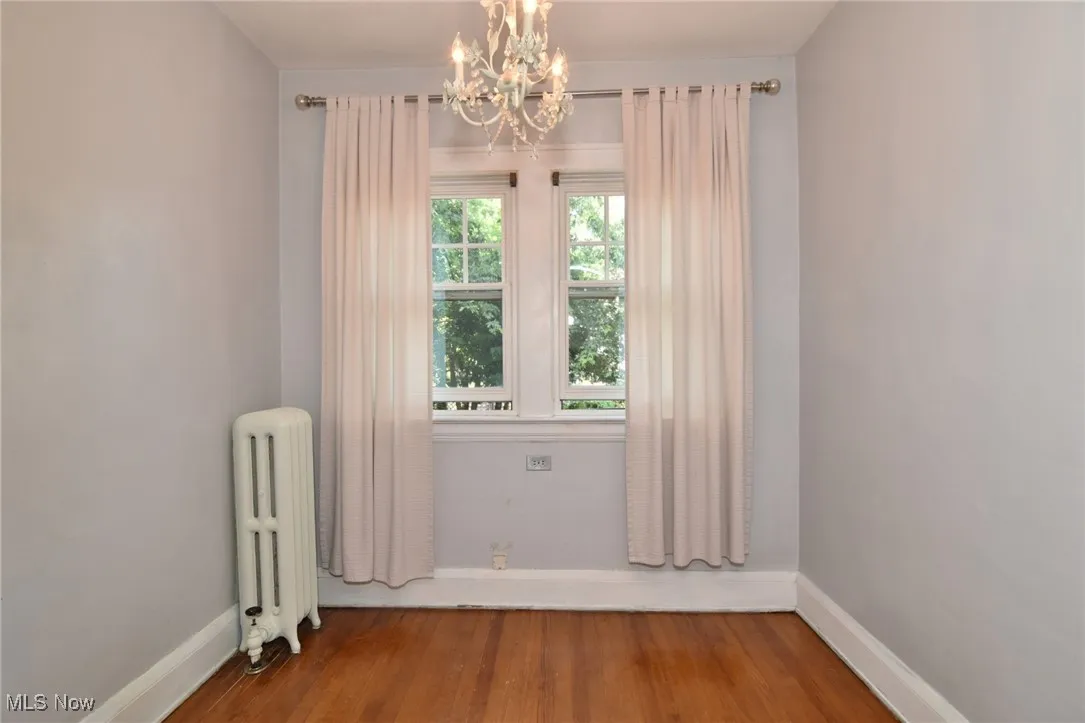 Unfurnished room featuring radiator heating unit, wood finished floors, and a chandelier