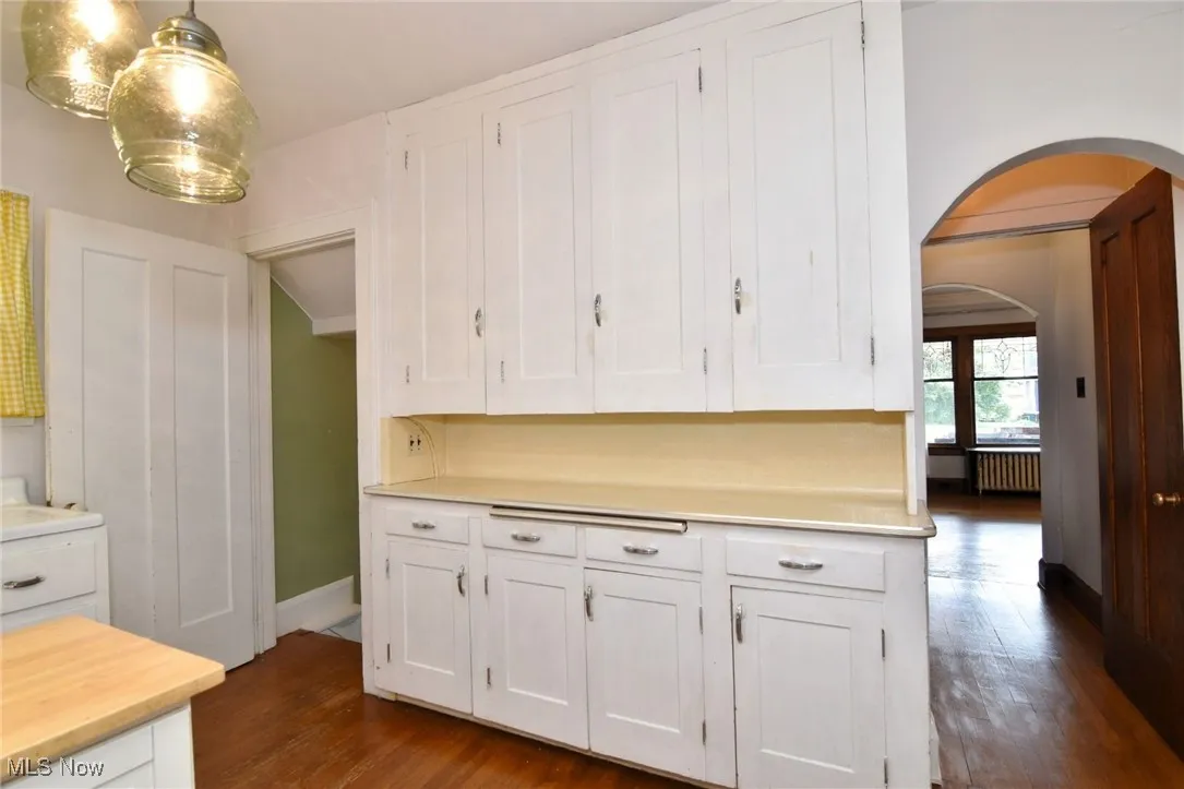 Kitchen with arched walkways, white cabinetry, light countertops, dark wood-style floors, and radiator