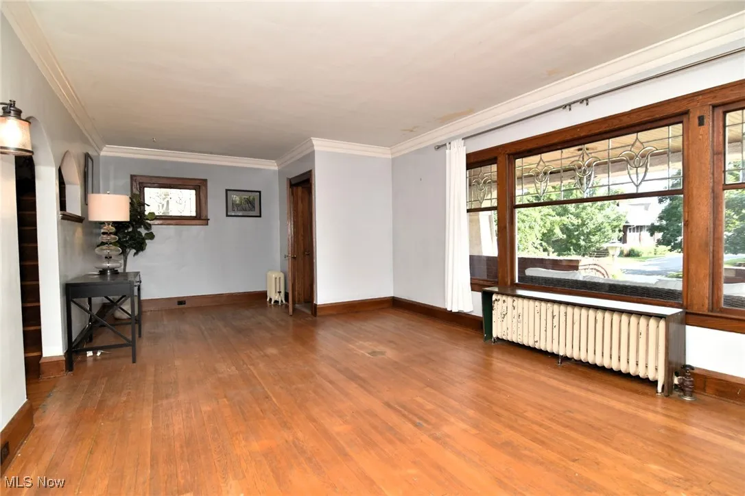 Empty room with radiator, plenty of natural light, wood finished floors, and crown molding