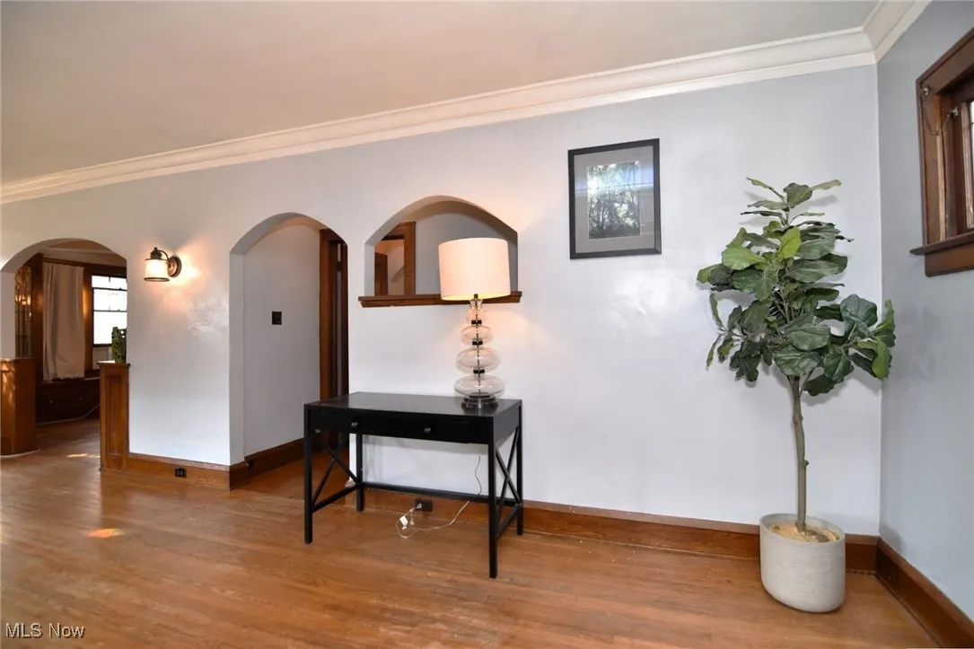 Hall with arched walkways, wood finished floors, and ornamental molding