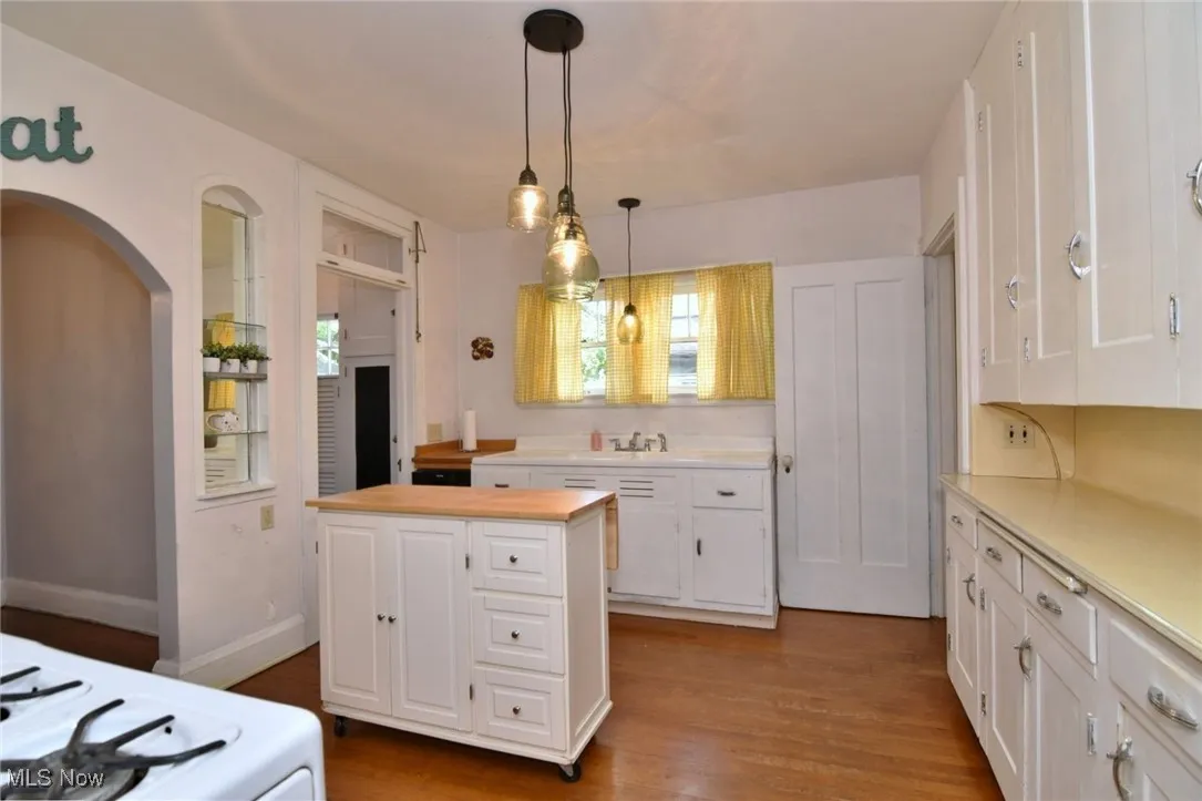 Kitchen featuring white cabinets, wood finished floors, hanging light fixtures, and a center island