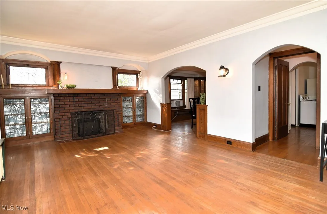 Unfurnished living room featuring wood finished floors, ornamental molding, a fireplace, arched walkways, and washer / dryer