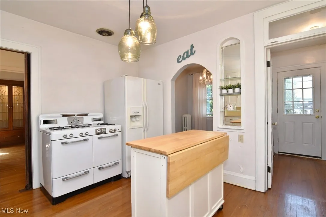 Kitchen with wooden counters, white appliances, wood finished floors, arched walkways, and white cabinets