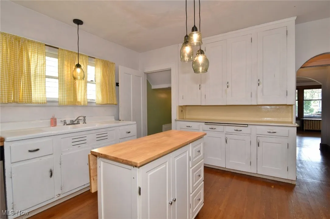 Kitchen featuring arched walkways, butcher block countertops, white cabinetry, wood finished floors, and hanging light fixtures
