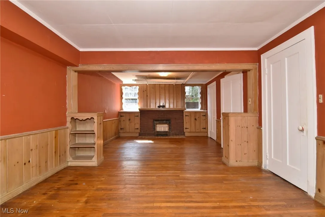 Bar area featuring wood finished floors, a fireplace, wooden walls, a wainscoted wall, and ornamental molding