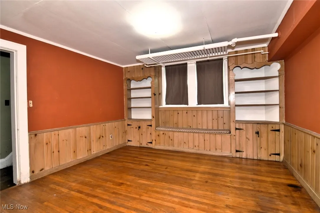 Empty room with wood finished floors, a wainscoted wall, wood walls, and crown molding
