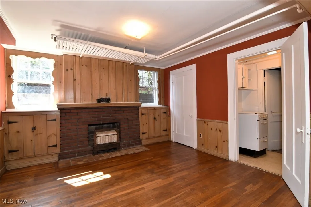 Unfurnished living room with wood finished floors, wooden walls, a brick fireplace, and ornamental molding
