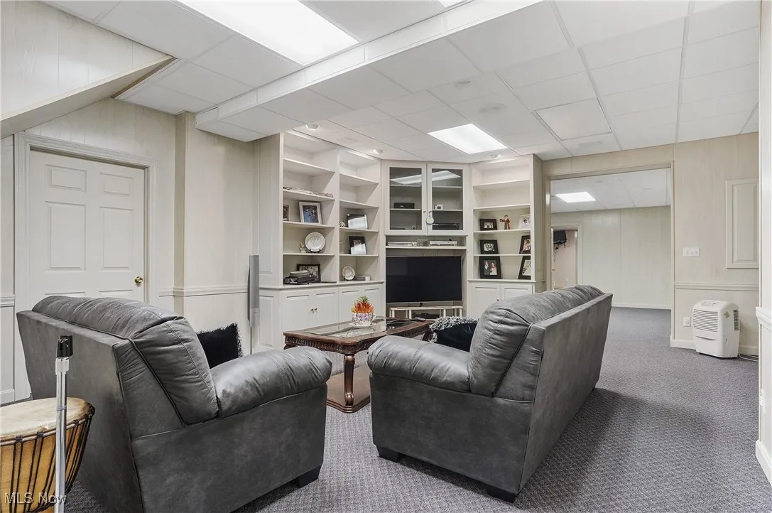 Carpeted living area featuring built in features, a drop ceiling, and a decorative wall