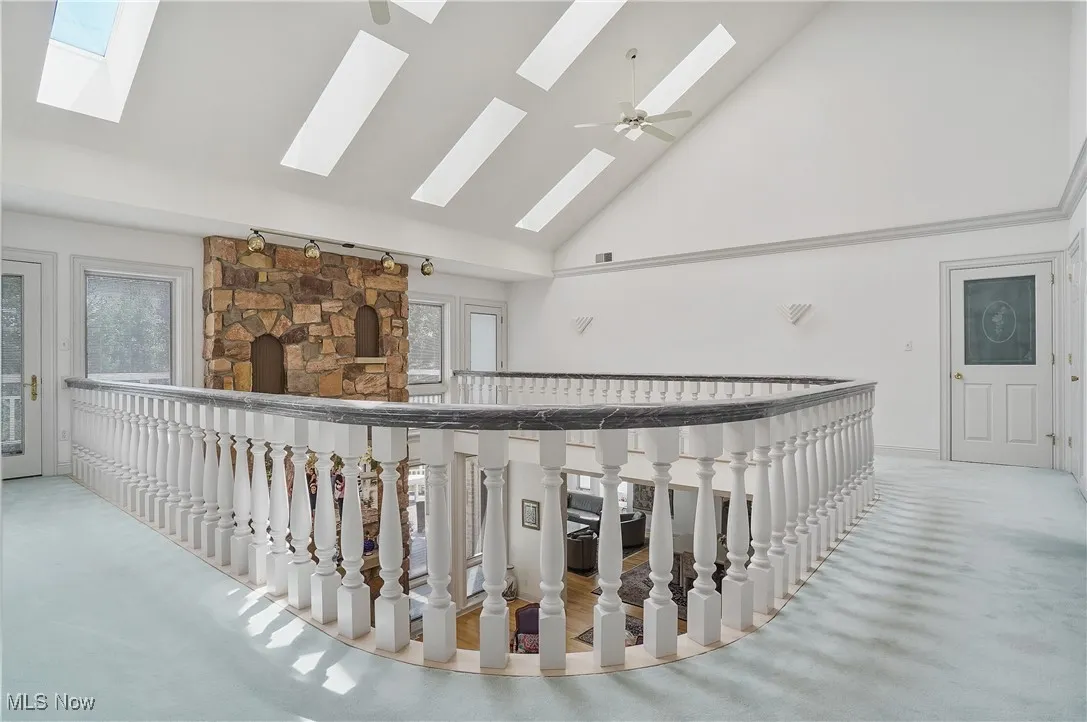 Hall with a skylight, high vaulted ceiling, healthy amount of natural light, and an upstairs landing