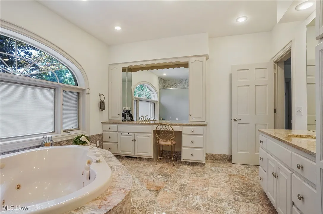 Full bathroom featuring two vanities, a tub with jets, and recessed lighting