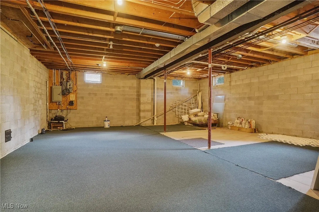 Basement with healthy amount of natural light, electric panel, and stairs
