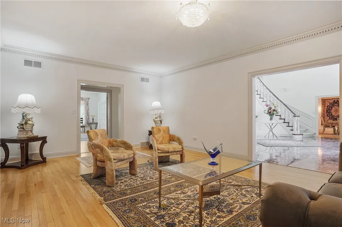 Living area with light wood-style floors, stairway, crown molding, and a chandelier
