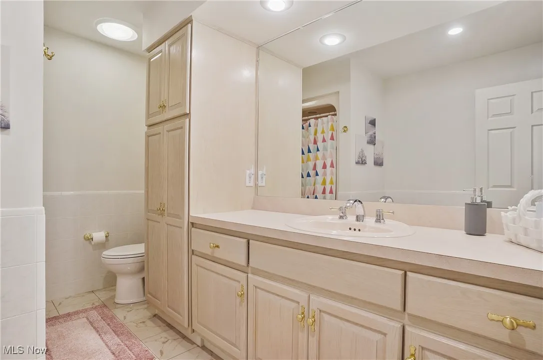 Bathroom with marble finish floors, vanity, recessed lighting, tile walls, and wainscoting
