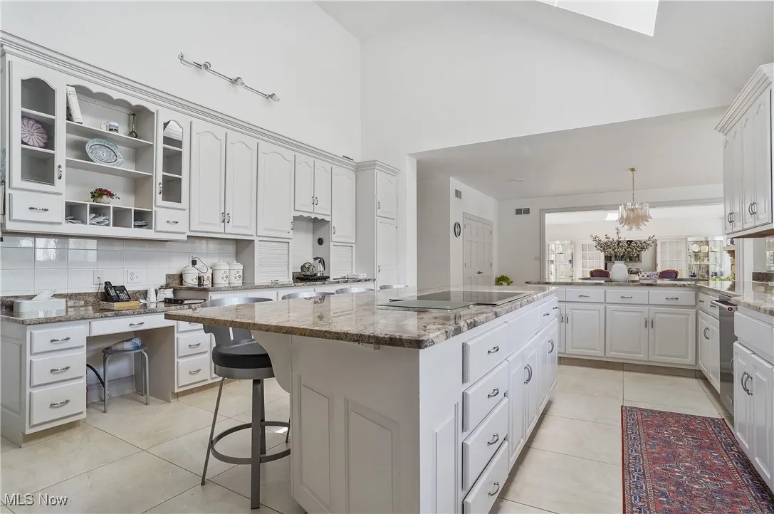 Kitchen with tasteful backsplash, high vaulted ceiling, a kitchen island, light tile patterned floors, and light stone counters