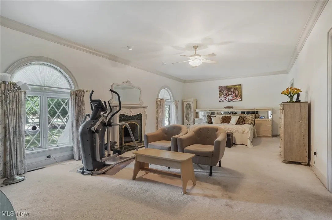 Bedroom featuring ornamental molding, light colored carpet, a fireplace, and a ceiling fan