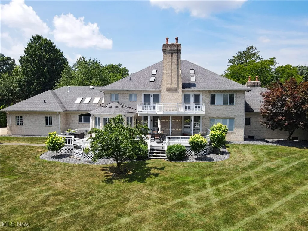 Rear view of property featuring a balcony, a chimney, a lawn, and a deck