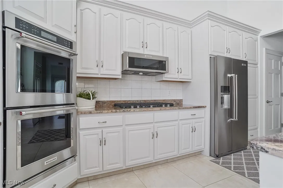 Kitchen featuring stainless steel appliances, backsplash, white cabinets, and light stone countertops