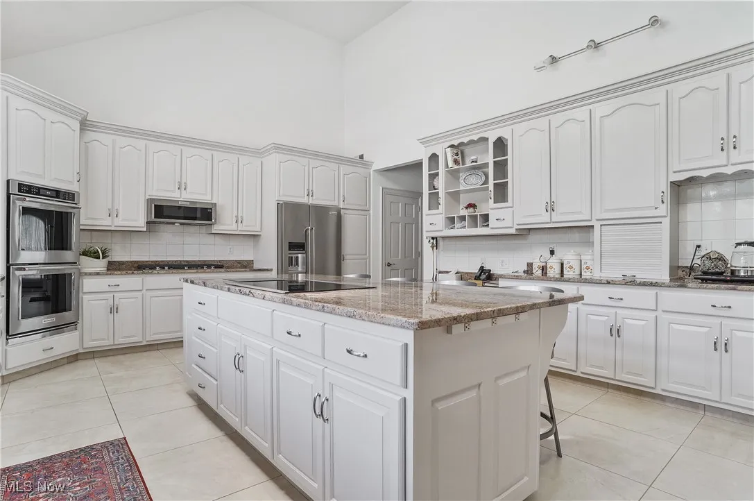 Kitchen featuring backsplash, high vaulted ceiling, a center island, appliances with stainless steel finishes, and light stone counters