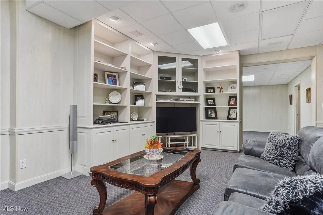 Living area featuring a paneled ceiling, dark carpet, and built in shelves