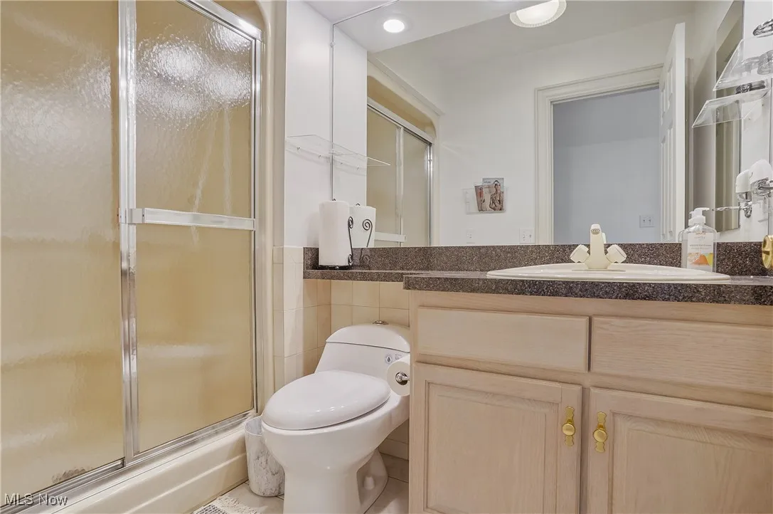 Bathroom with a shower with shower door, vanity, tile walls, and recessed lighting