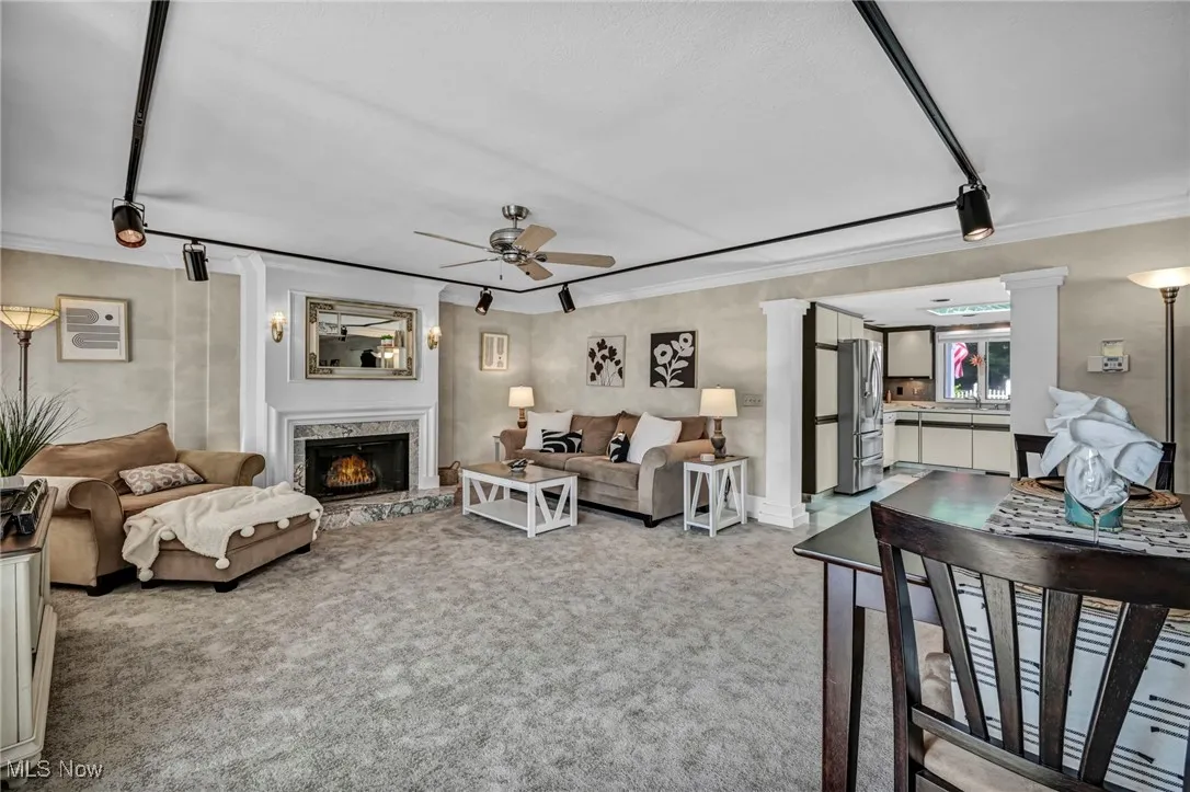 Living area featuring ornamental molding, carpet flooring, a ceiling fan, decorative columns, and a fireplace