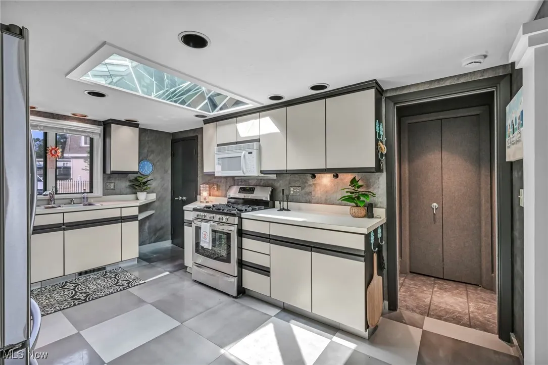 Kitchen with stainless steel appliances, light countertops, a skylight, and white cabinetry