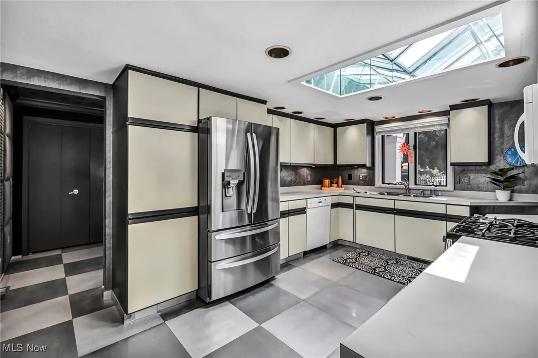 Kitchen with a skylight, stainless steel fridge, light countertops, light flooring, and tasteful backsplash