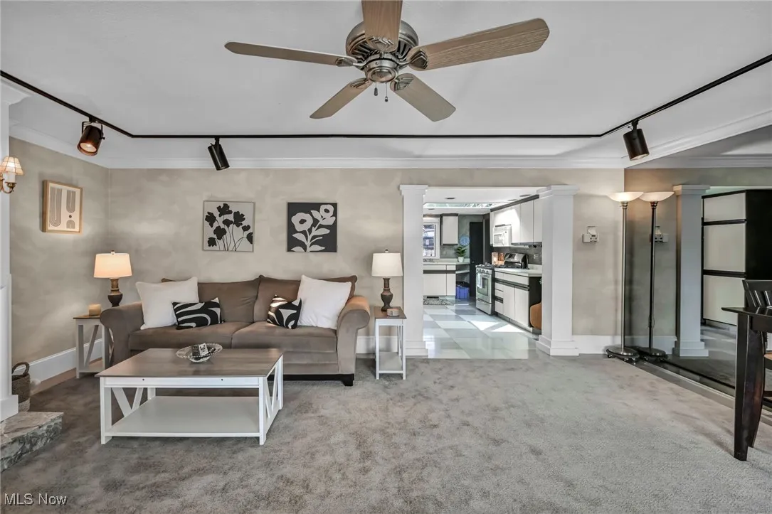 Living room featuring rail lighting, a ceiling fan, light carpet, ornamental molding, and ornate columns