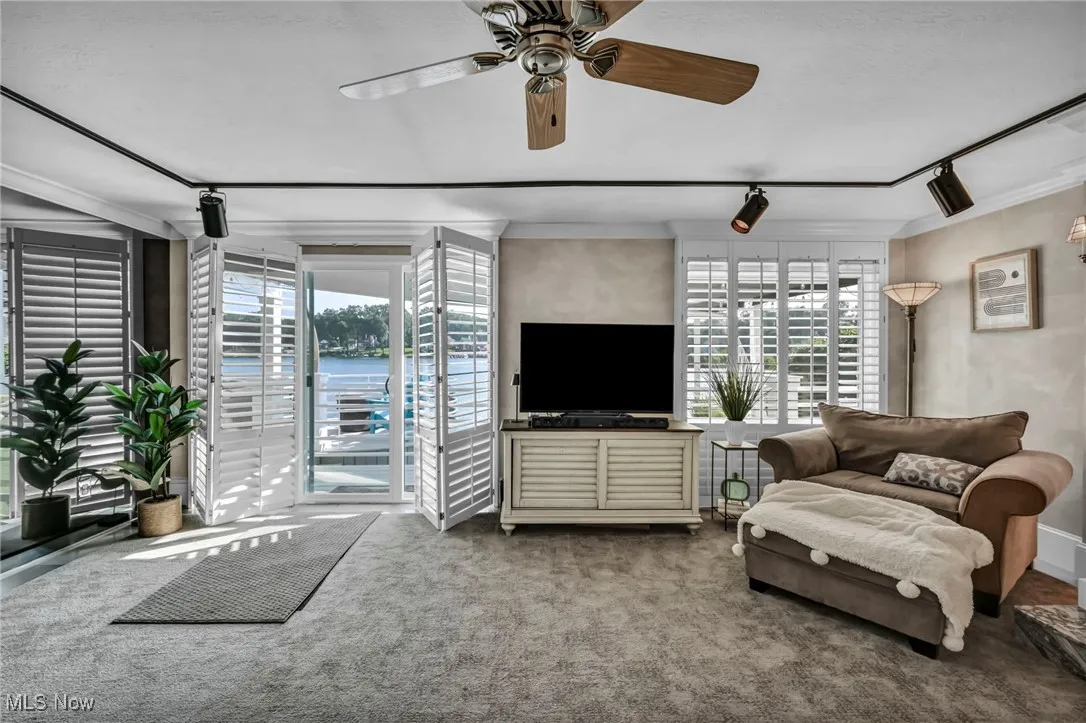 Living room with a ceiling fan, carpet, crown molding, and track lighting