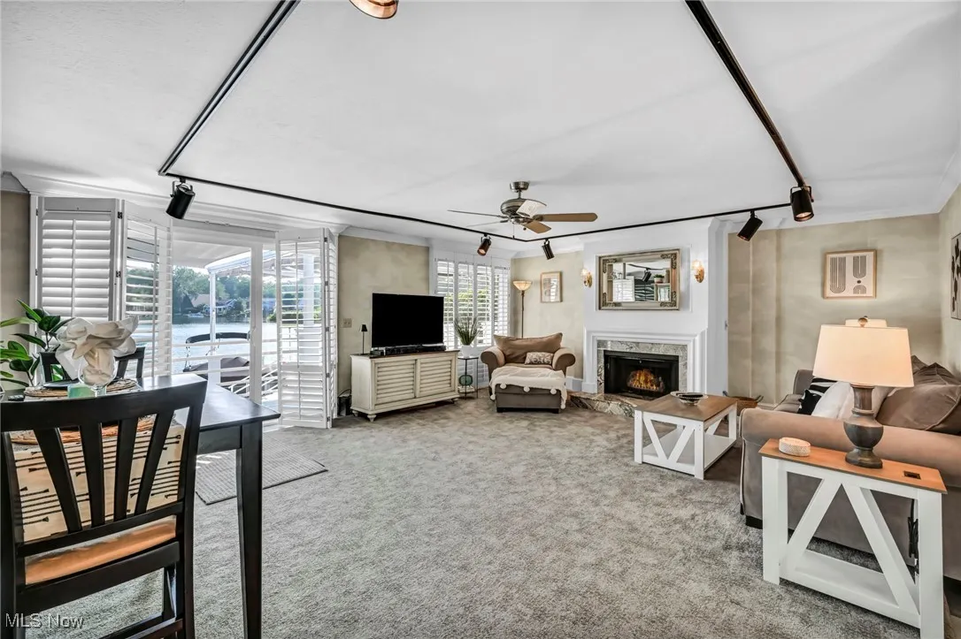 Carpeted living area featuring a ceiling fan, a fireplace, crown molding, and rail lighting