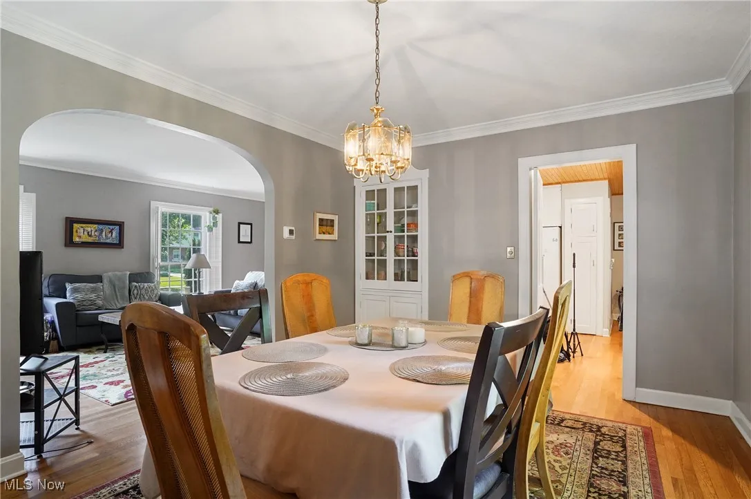 Dining area with arched walkways, a chandelier, crown molding, and light wood-style flooring