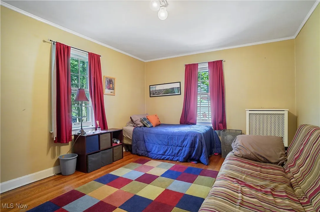 Bedroom with wood finished floors, multiple windows, and ornamental molding