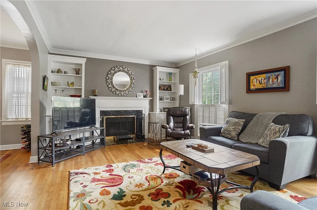 Living area featuring built in shelves, crown molding, wood finished floors, a premium fireplace, and arched walkways