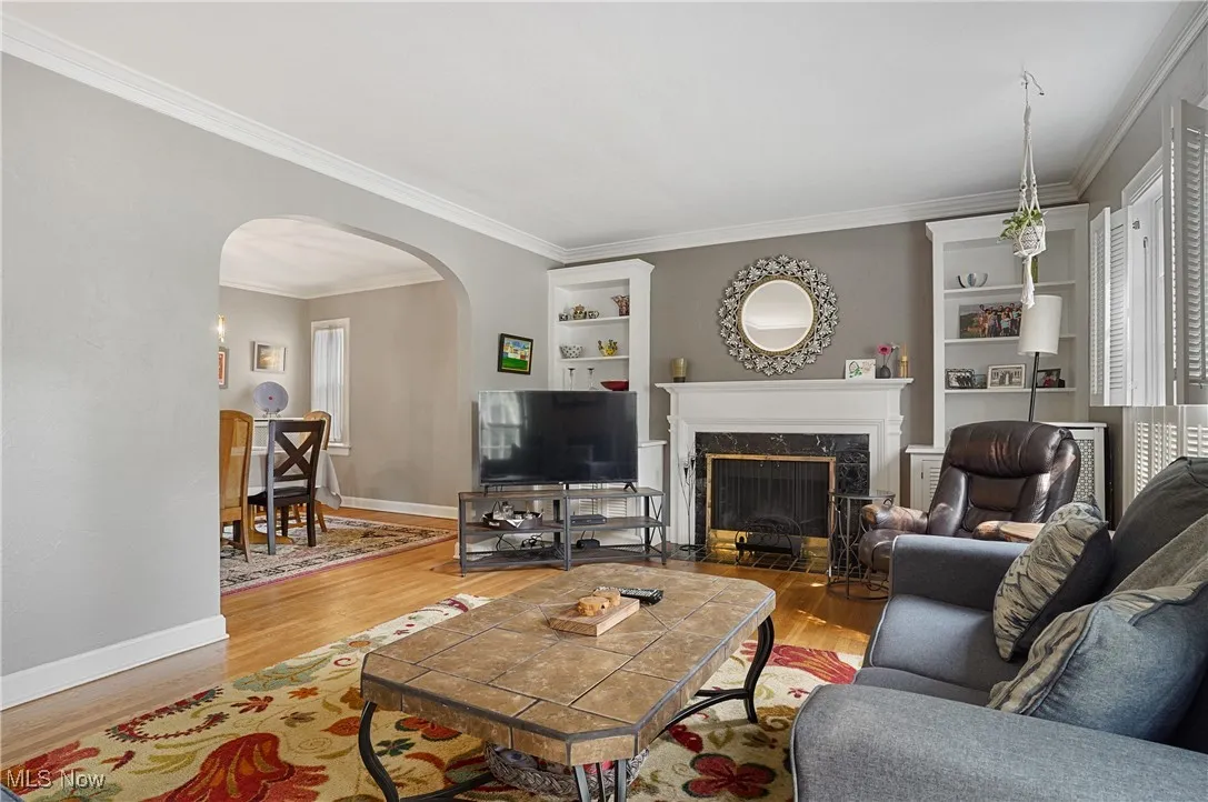 Living area with arched walkways, crown molding, wood finished floors, a premium fireplace, and built in features