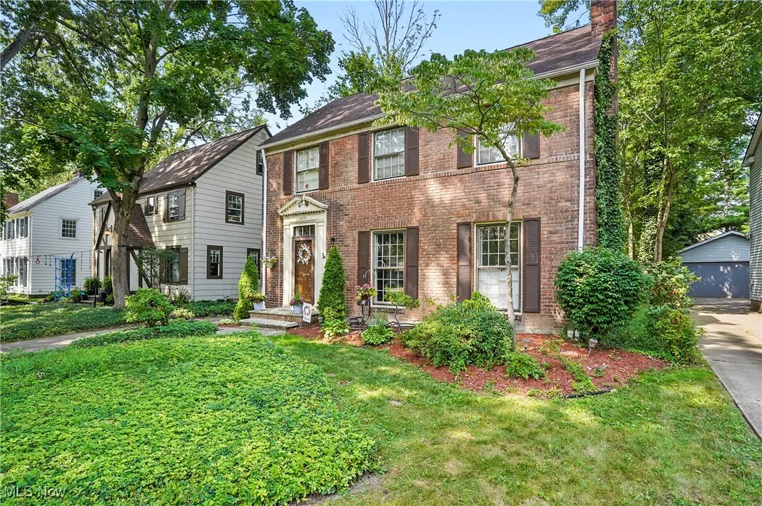 Colonial inspired home with brick siding, a front lawn, an outbuilding, and a chimney