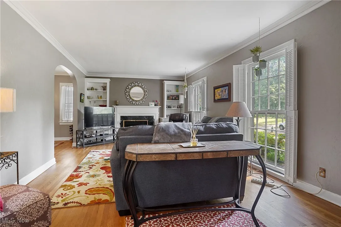 Living area with ornamental molding, arched walkways, built in features, light wood-style flooring, and a premium fireplace