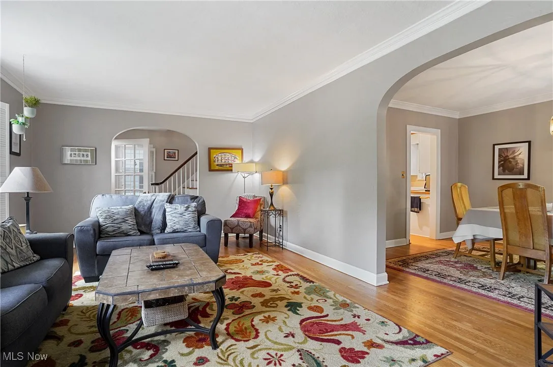 Living room with arched walkways, wood finished floors, crown molding, and stairway