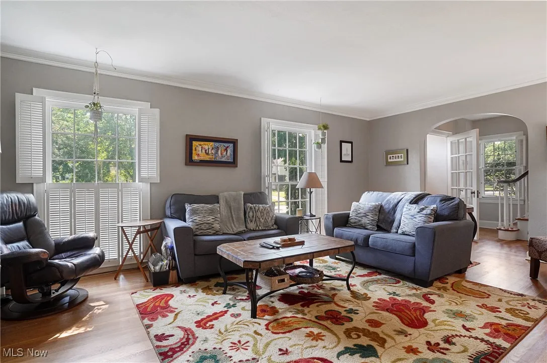 Living room with arched walkways, wood finished floors, and crown molding