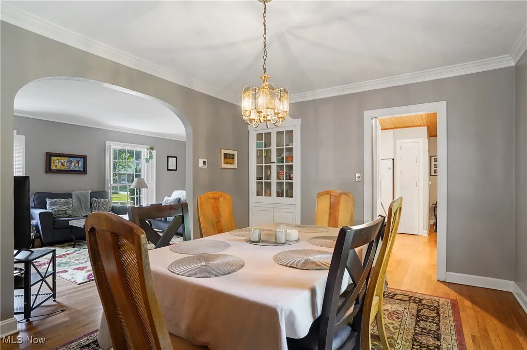 Dining space featuring arched walkways, a chandelier, light wood-type flooring, and crown molding