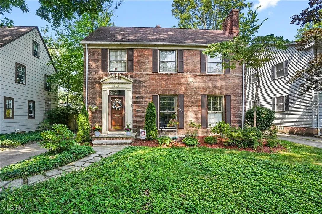 Colonial-style house featuring brick siding, a chimney, a front lawn, and roof with shingles