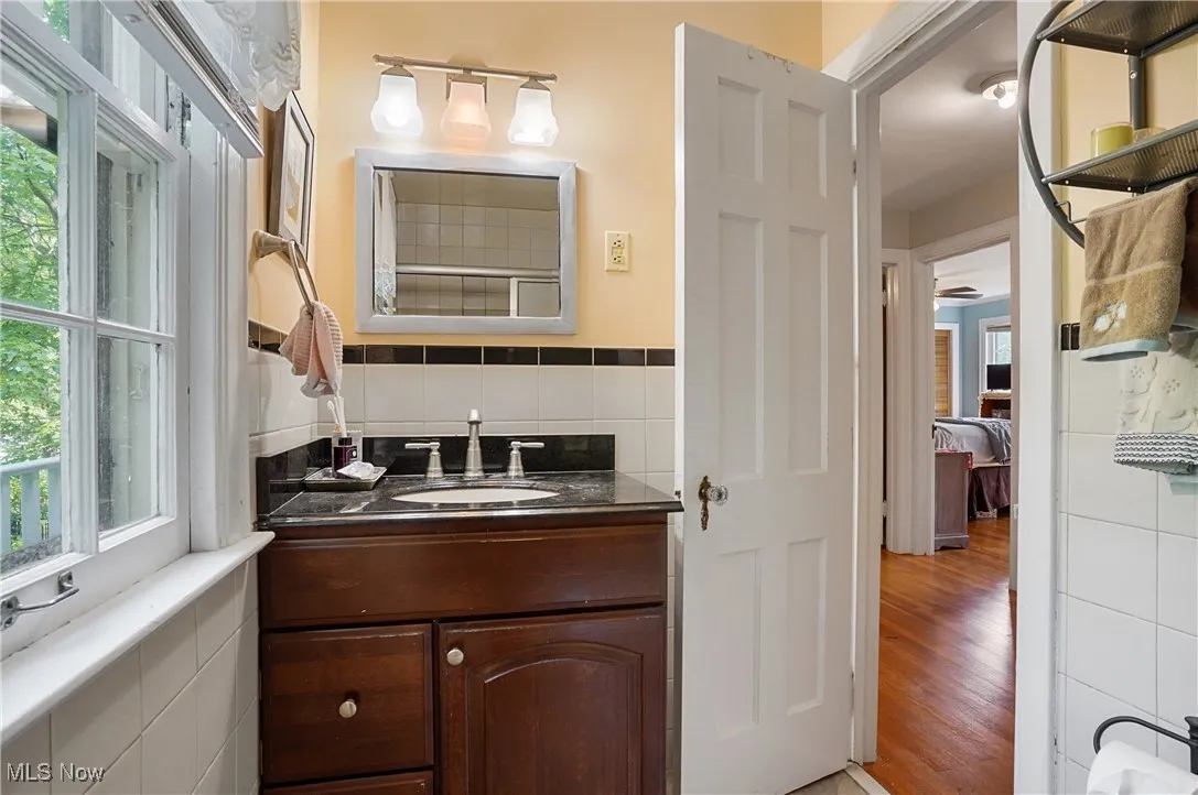 Ensuite bathroom featuring vanity, wood finished floors, and tile walls