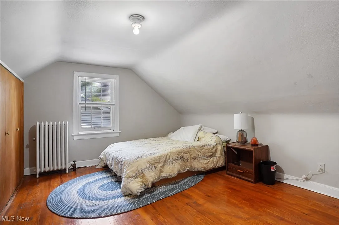 Bedroom featuring radiator heating unit, wood finished floors, and lofted ceiling
