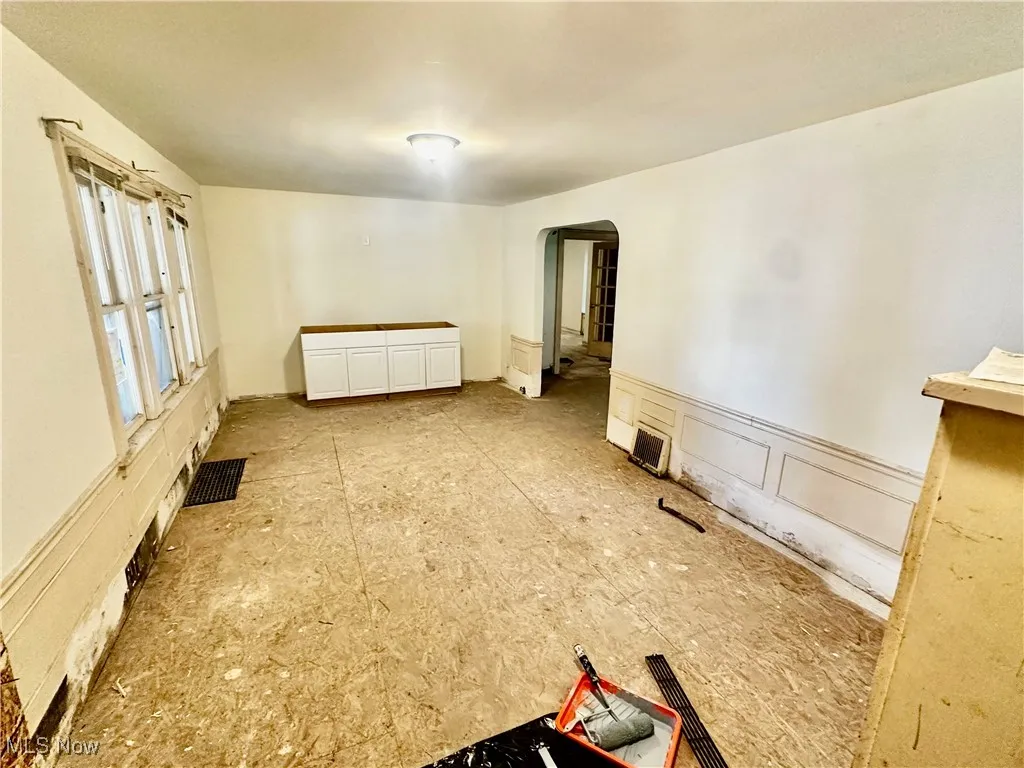 Empty room featuring arched walkways, a decorative wall, and a wainscoted wall
