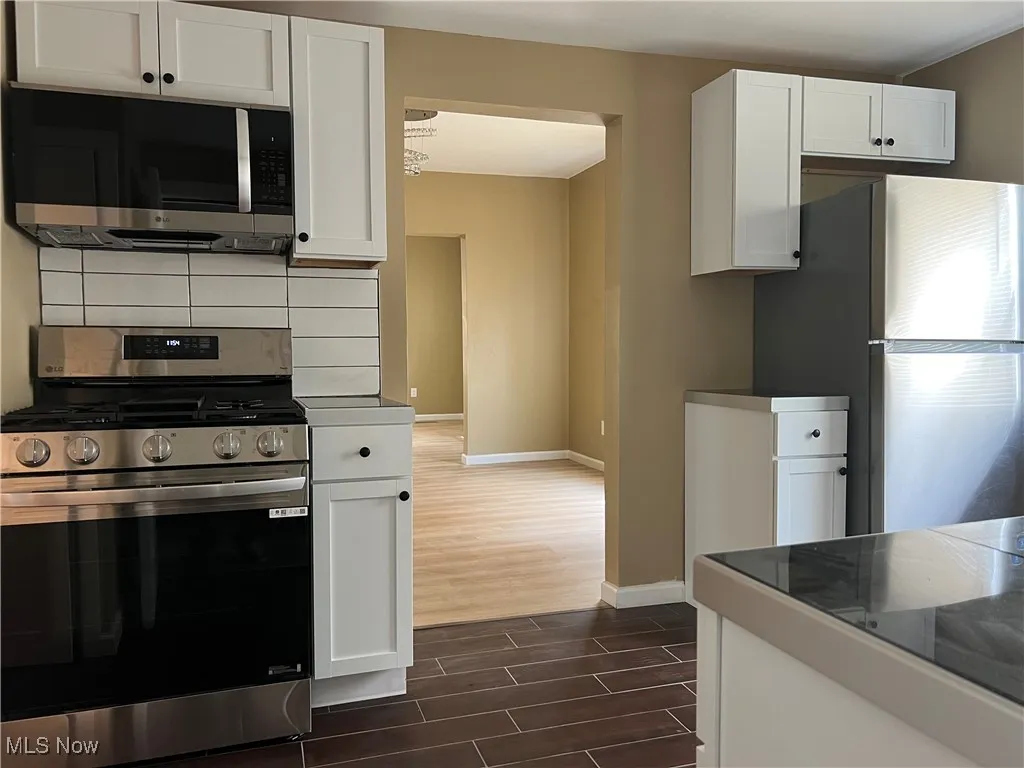 Kitchen featuring appliances with stainless steel finishes, wood tiled floors, white cabinetry, and backsplash
