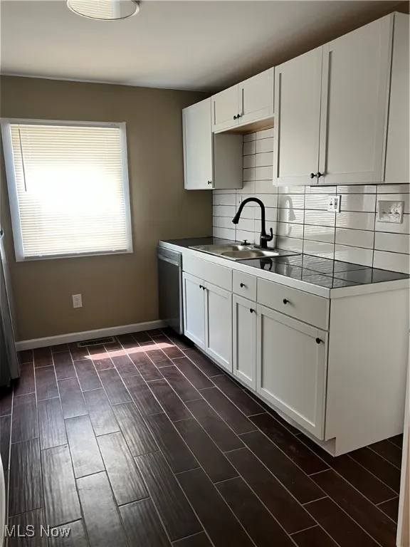 Kitchen with decorative backsplash, white cabinetry, dishwasher, and dark wood finished floors
