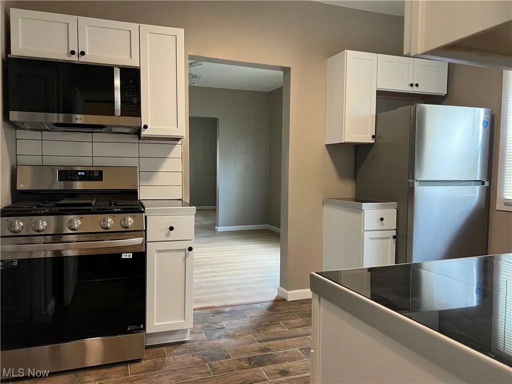 Kitchen with stainless steel appliances, white cabinets, dark wood finished floors, and dark countertops