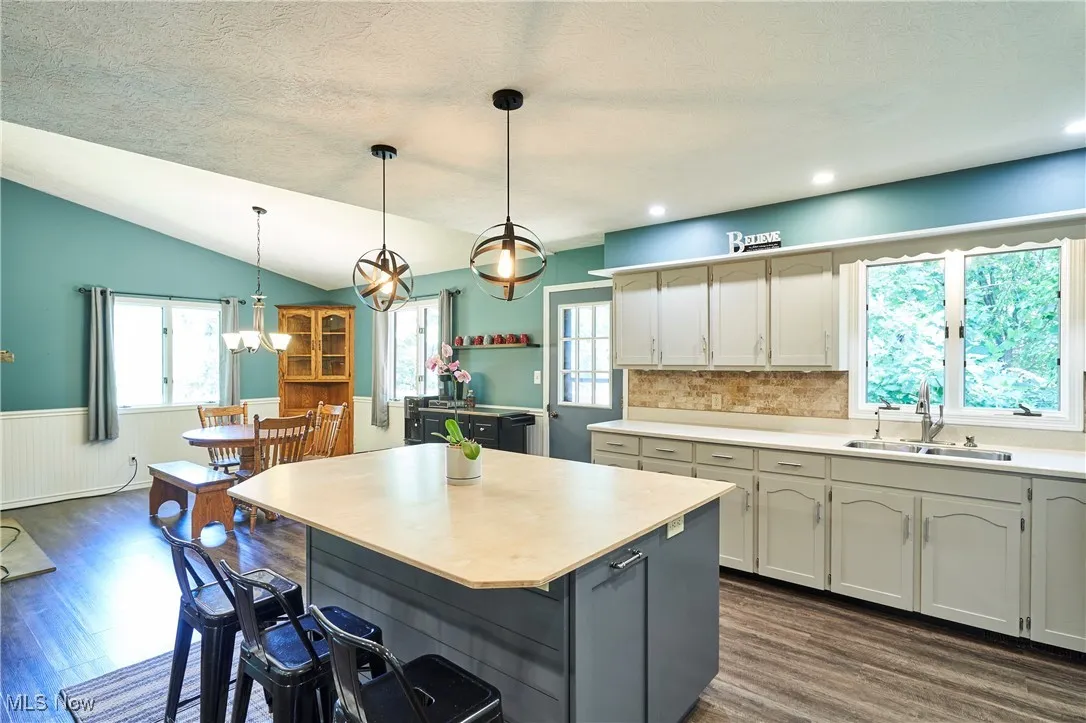Kitchen featuring a kitchen breakfast bar, dark wood-style flooring, light countertops, lofted ceiling, and wainscoting