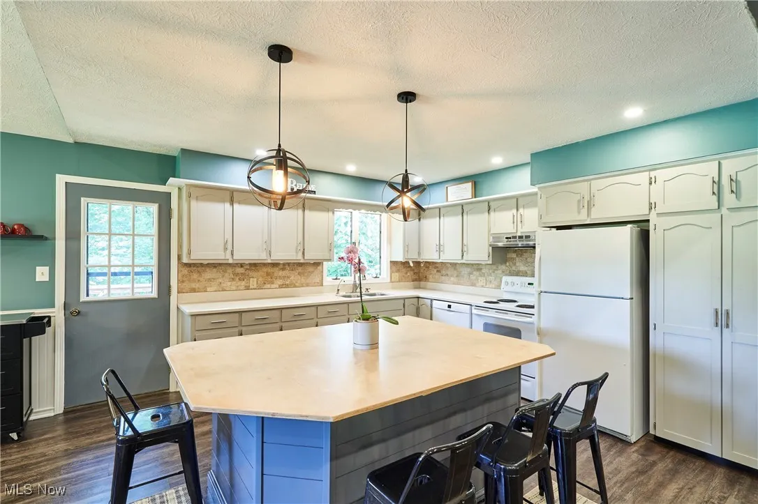 Kitchen with white appliances, a kitchen breakfast bar, light countertops, dark wood-style flooring, and a textured ceiling